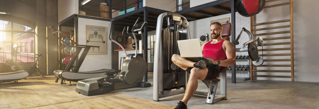 promocja konta firmowego w Santander. Na obrazku umięśniony mężczyzna na siłowni z laptopem na kolanach.